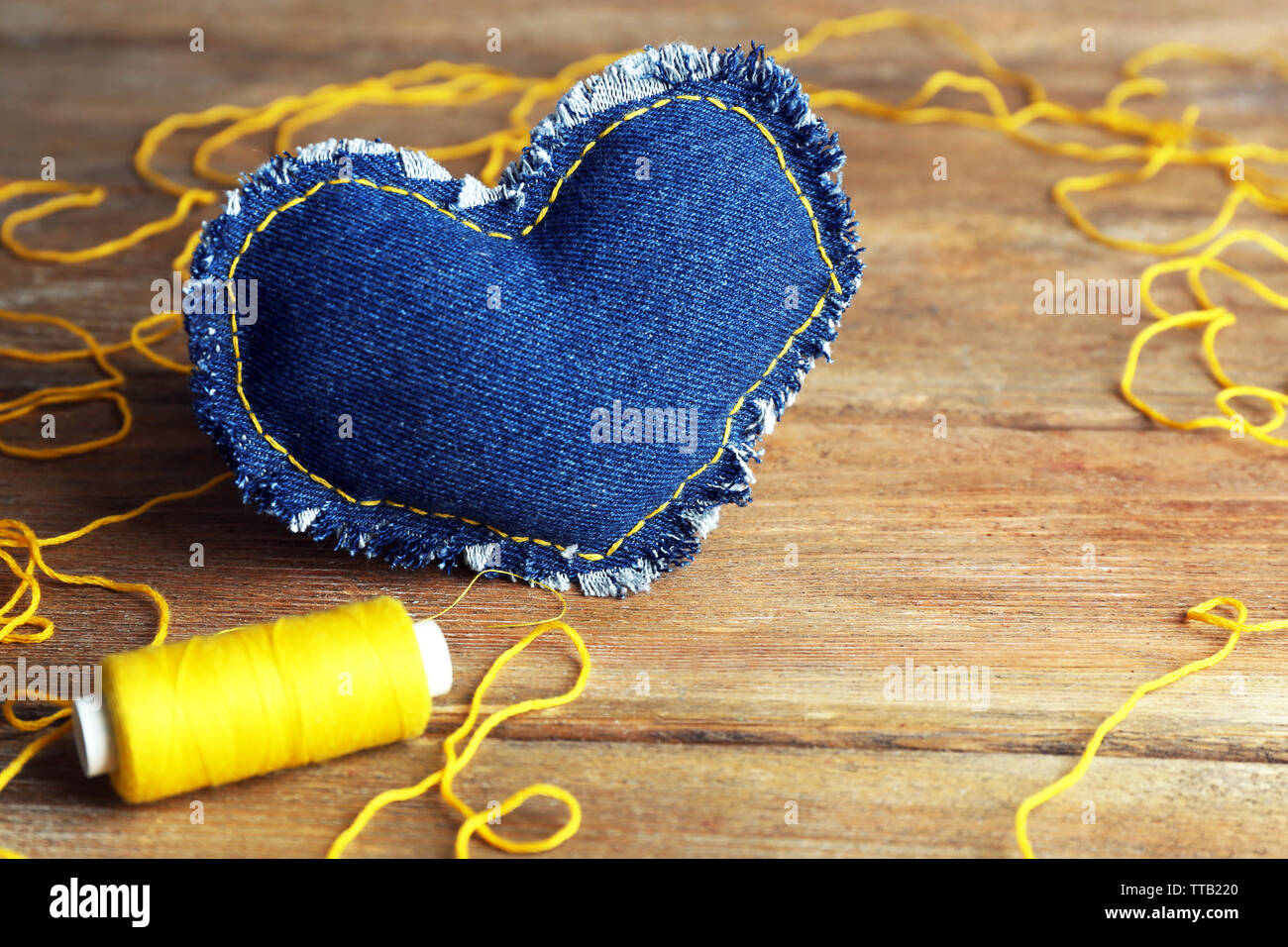 Denim heart and thread on wooden background Stock Photo