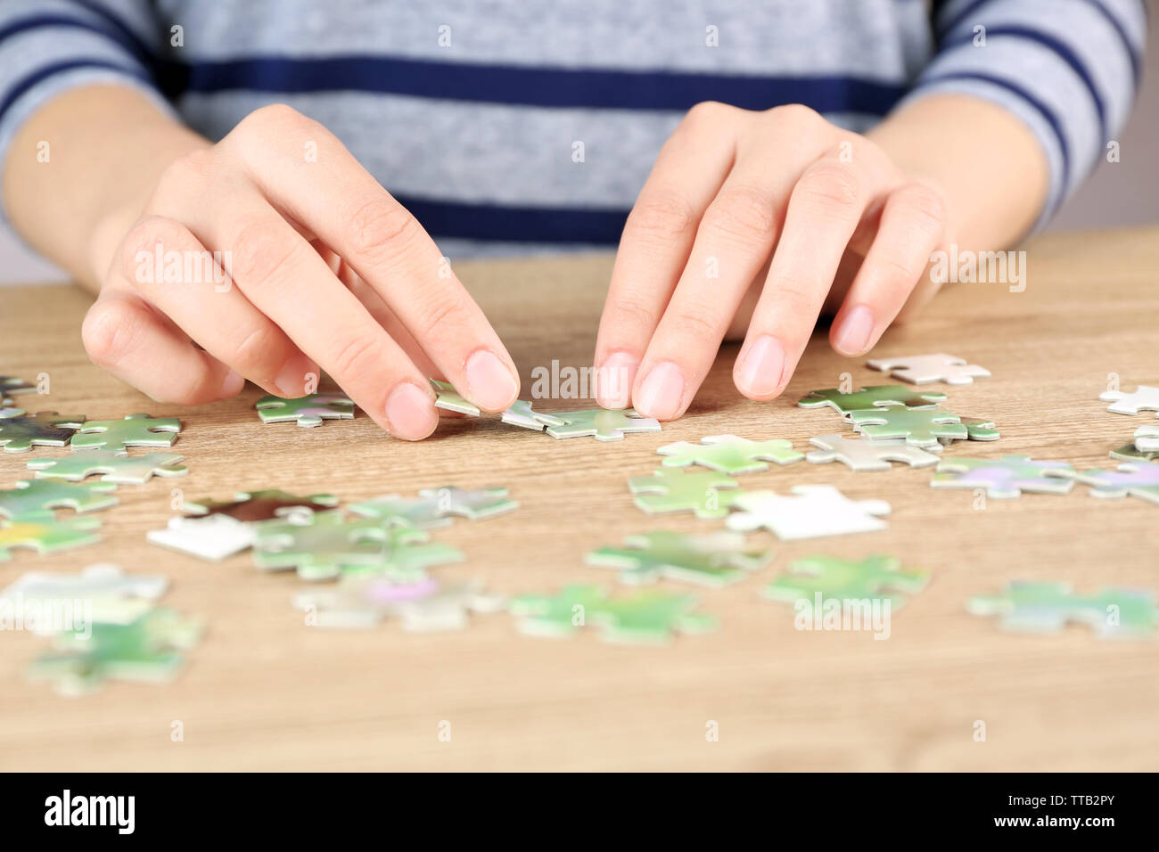 Female hands assembling puzzle on wooden table, closeup Stock Photo