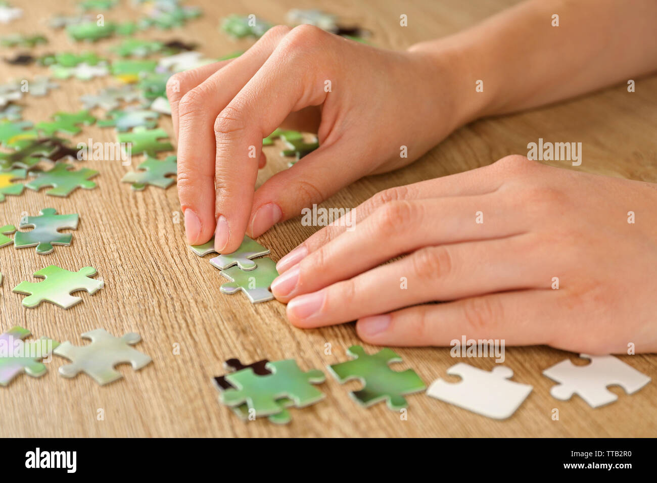Female hands assembling puzzle on wooden table, closeup Stock Photo