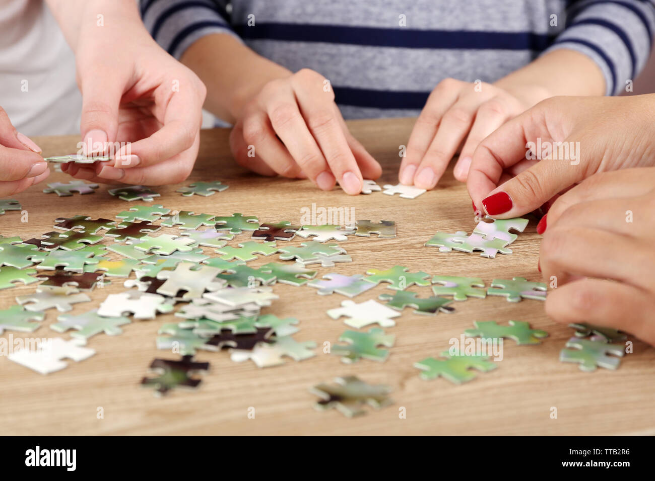 Female hands assembling puzzle on wooden table, closeup Stock Photo