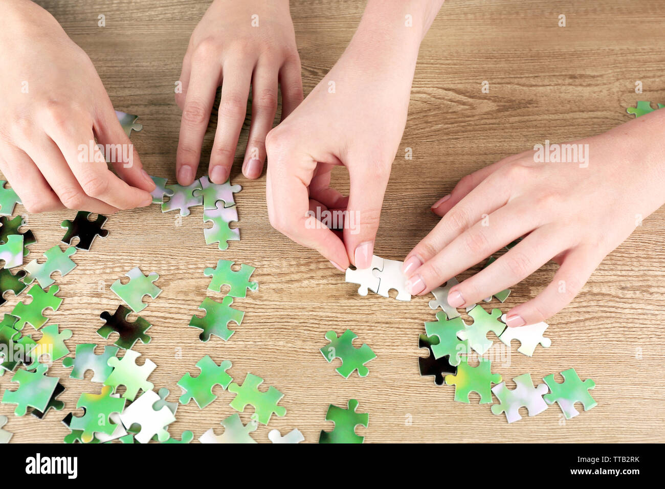 Female hands assembling puzzle on wooden table, closeup Stock Photo