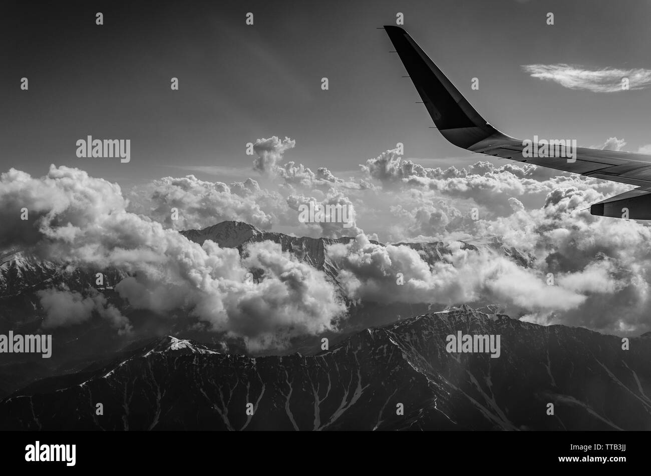 Black and white photograph of the mesmerising Himalayan mountains peaking through clouds on a cloudy day of flight from Delhi to Srinagar. Stock Photo