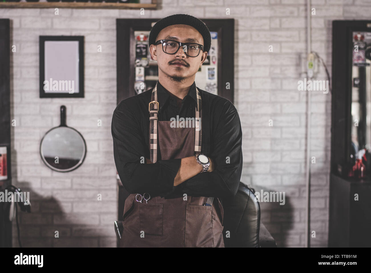 Barber man hairstylist  posing and standing with apron crossed his arm at barbershop salon Stock Photo