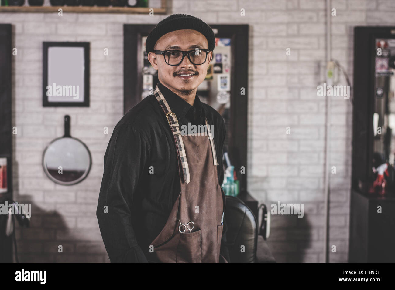portrait of happy Barber man hairstylist  posing and standing with apron crossed his arm at barbershop salon Stock Photo