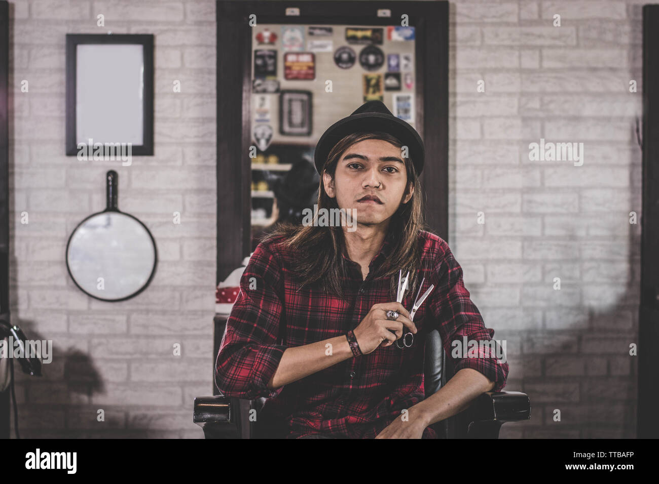https://c8.alamy.com/comp/TTBAFP/portrait-of-confident-young-long-hair-stylist-barber-sitting-at-vintage-barbershop-chair-holding-twos-scissor-facing-and-looking-at-camera-TTBAFP.jpg