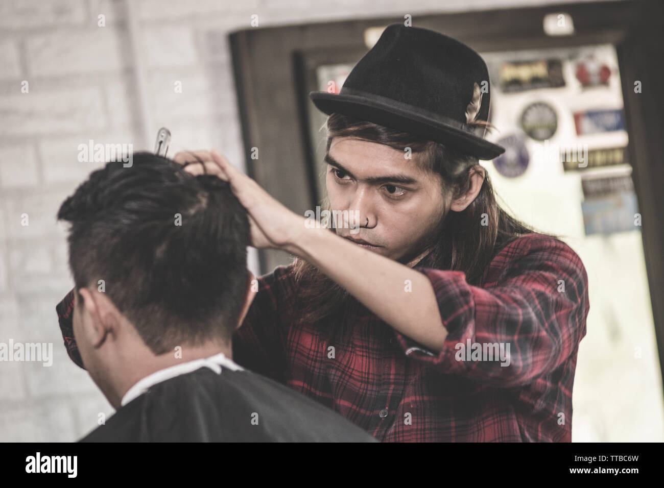 portrait of professional Asian man with long brown hair work as barber trimming his costumer with scissors and comb in barbershop Stock Photo