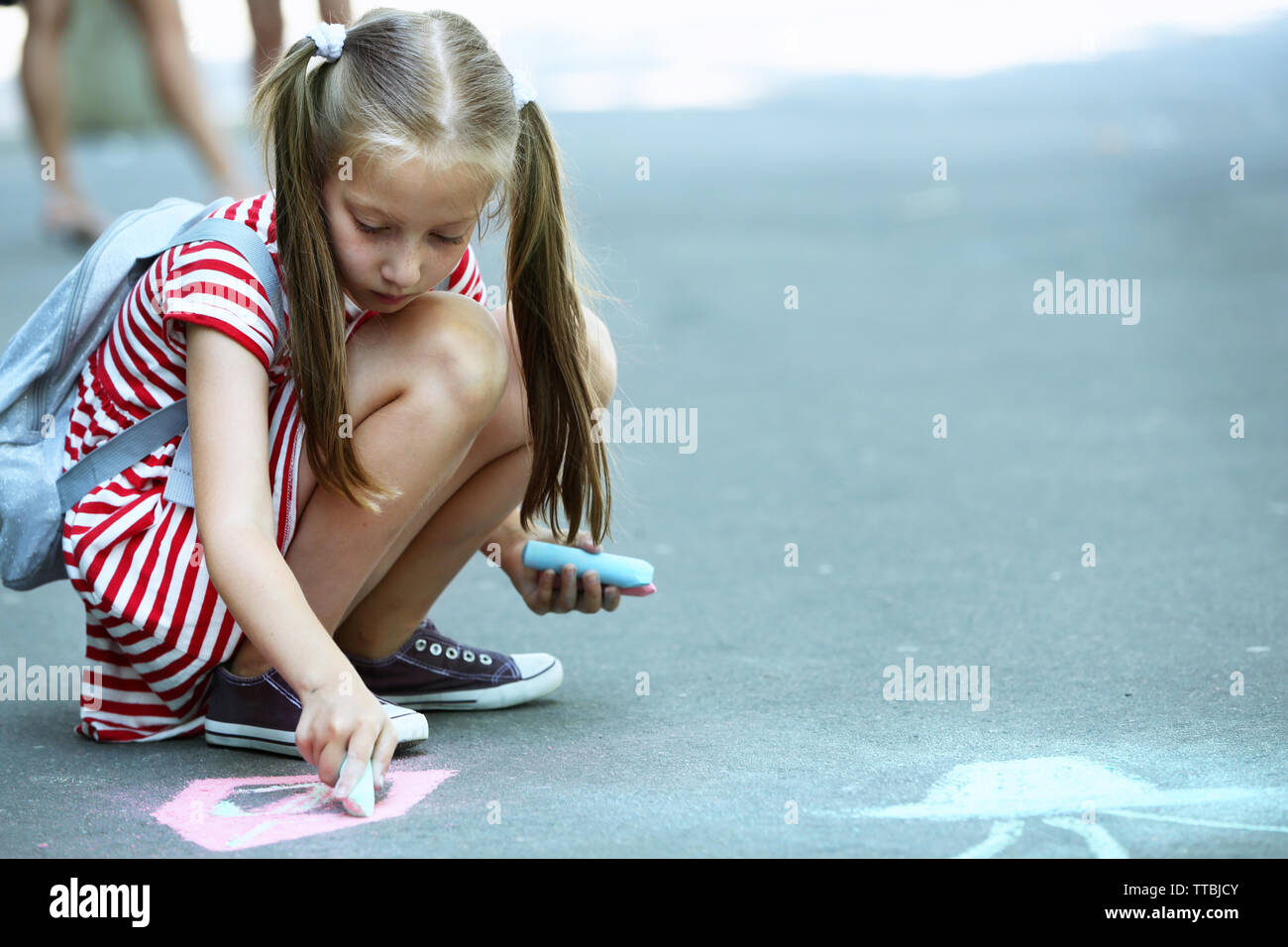 Cute small girl drawing with chalk on asphalt Stock Photo - Alamy