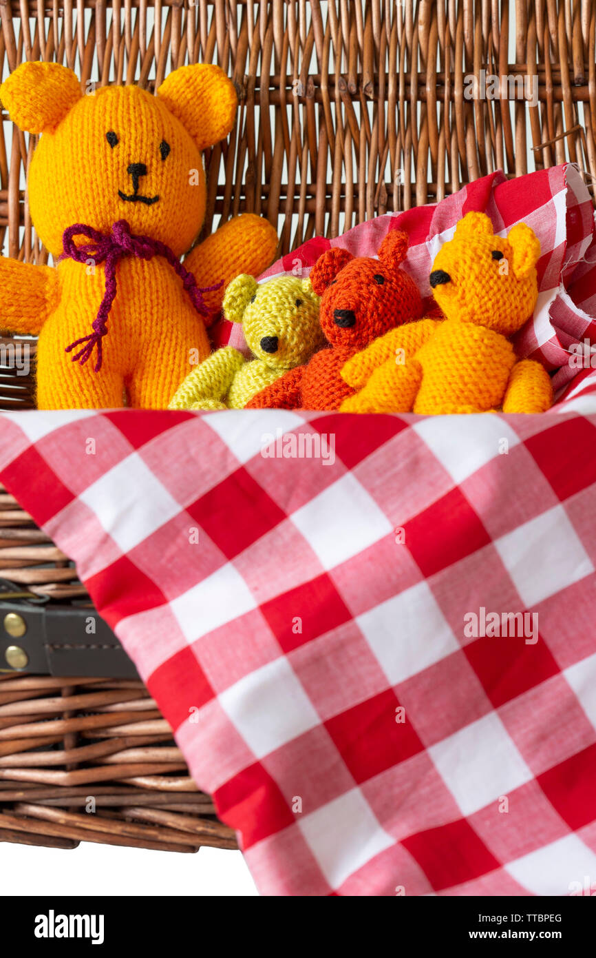 Knitted teddy bear toys on gingham fabric material in a wicker picnic