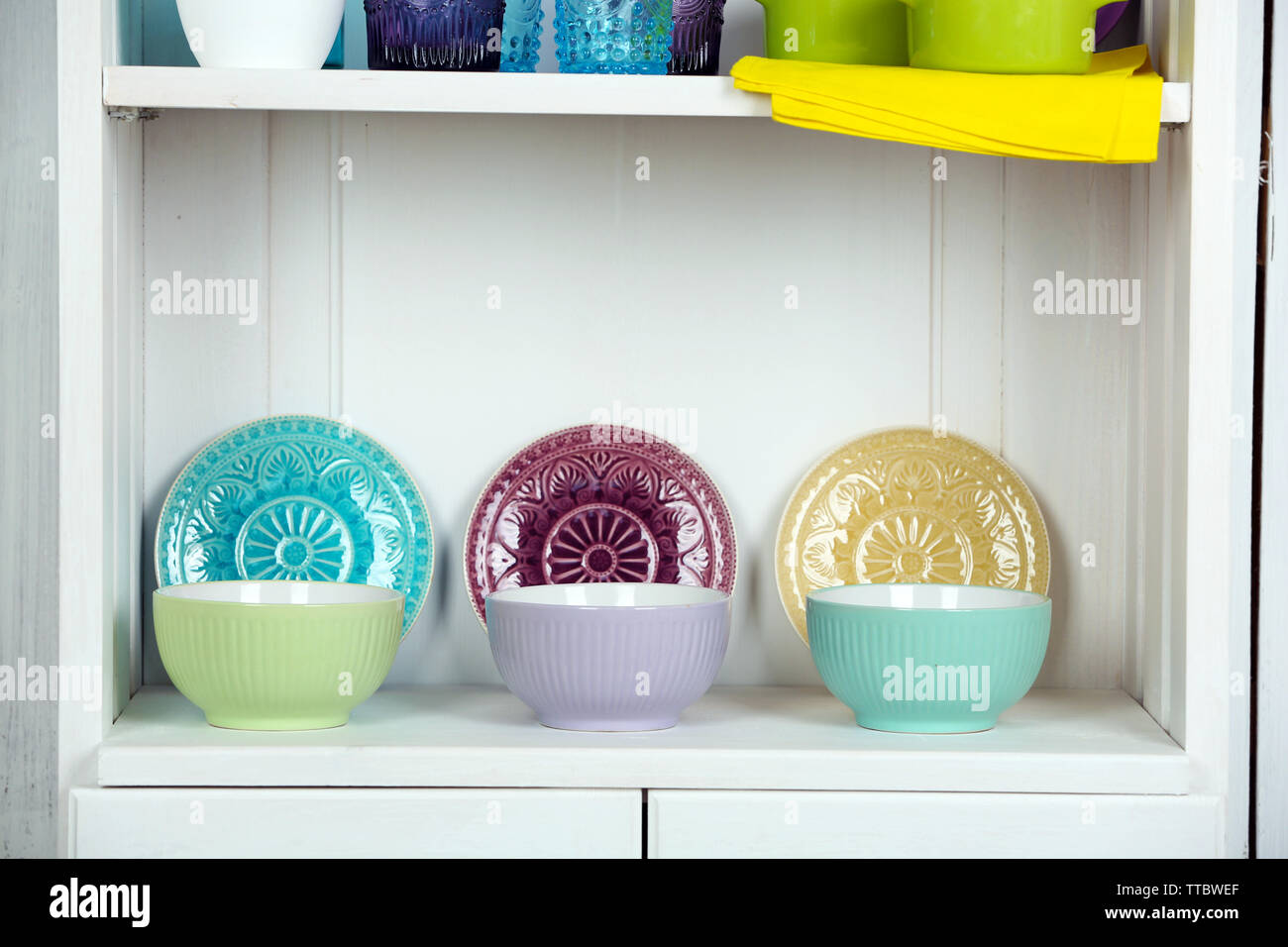 Clean glasses, plates and cutlery on shelf in kitchen cupboard Stock