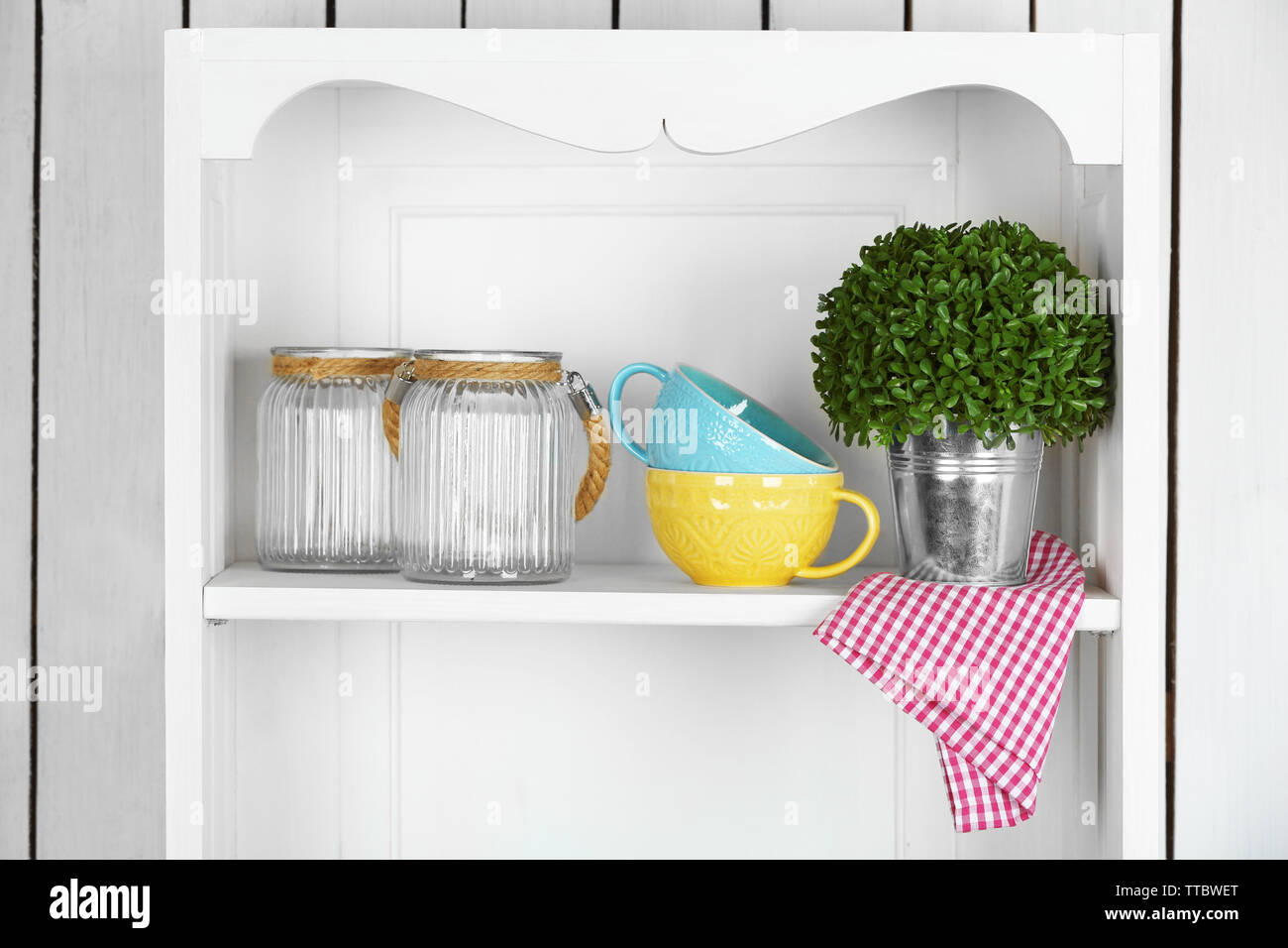 Clean glasses, plates and cutlery on shelf in kitchen cupboard Stock