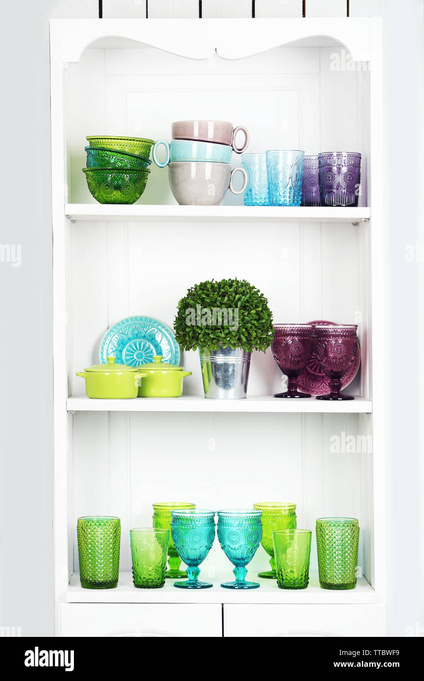 Clean glasses, plates and cutlery on shelves in kitchen cupboard Stock