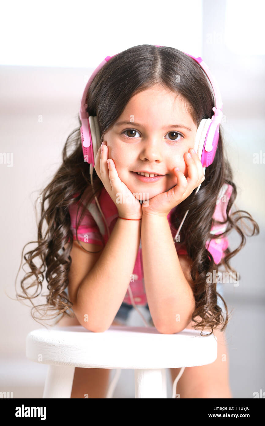 Pretty smiling little girl listening music with pink headphones in