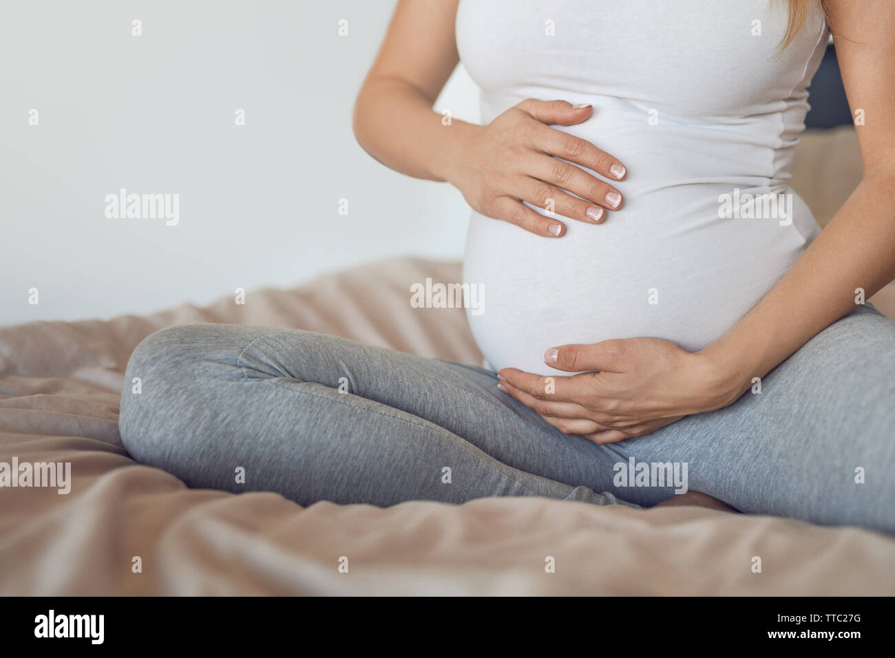 Young pregnant woman cradling her baby bump or belly with her hands in a close up cropped view conceptual of maternal love Stock Photo