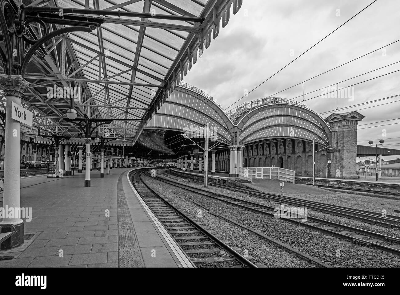 York Railway station where two19th Century canopies of iron and glass cover the platforms.  The platform curves into the station and a cloudy sky is a Stock Photo