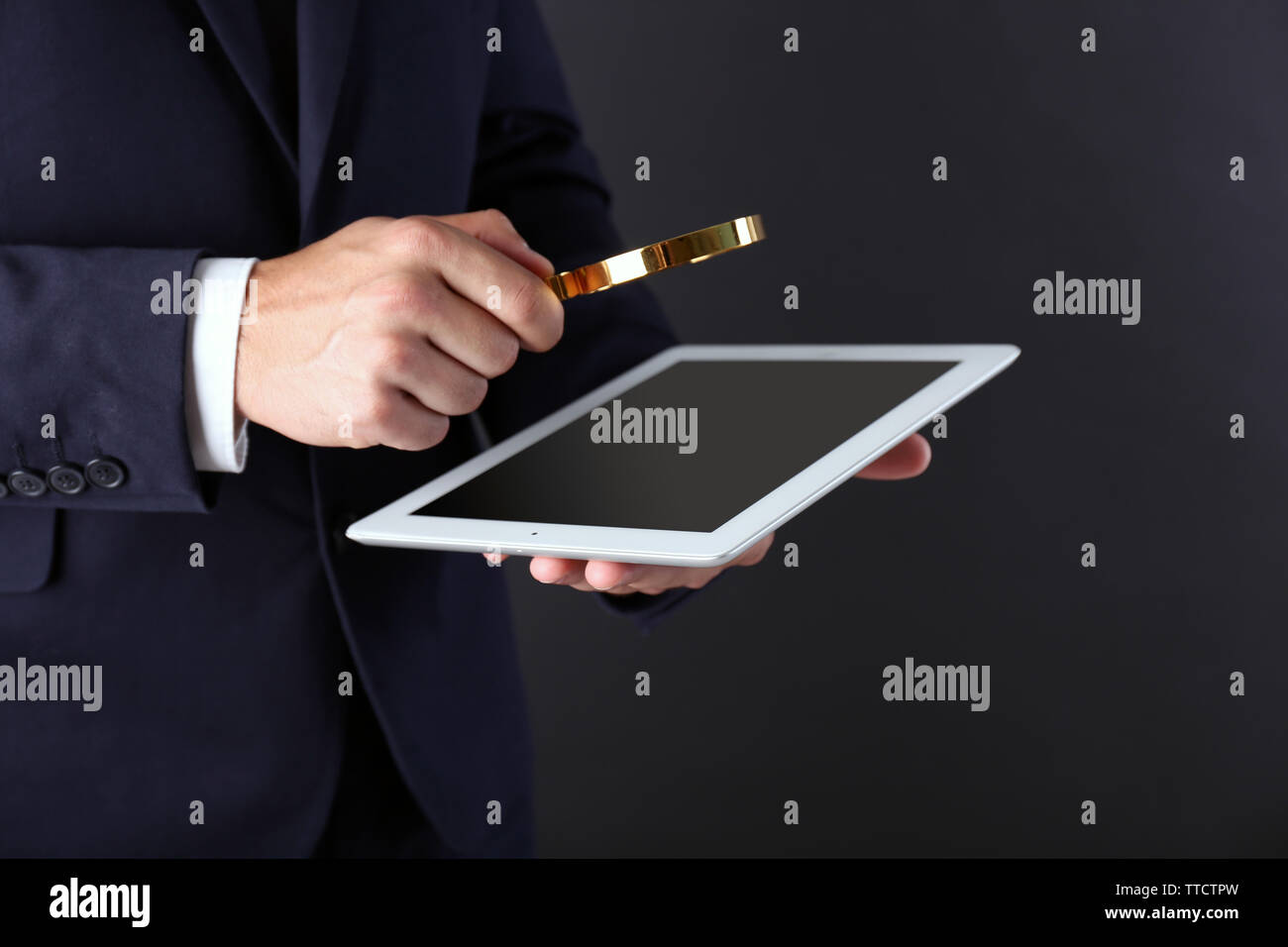Businessman holding magnifying glass and digital tablet on dark grey