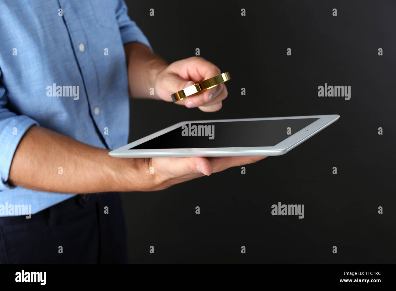 Businessman holding magnifying glass and digital tablet on dark grey