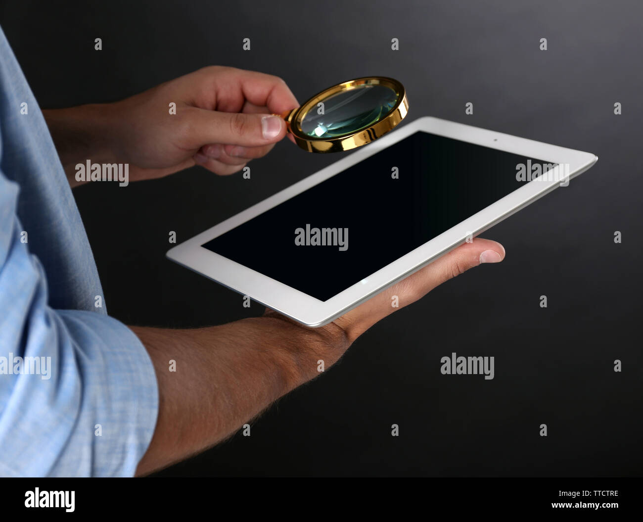 Businessman holding magnifying glass and digital tablet on dark grey