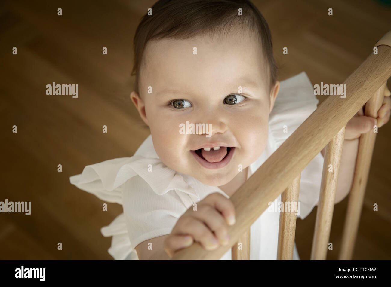 Cute little baby girl holding onto the top of safety gate Stock Photo