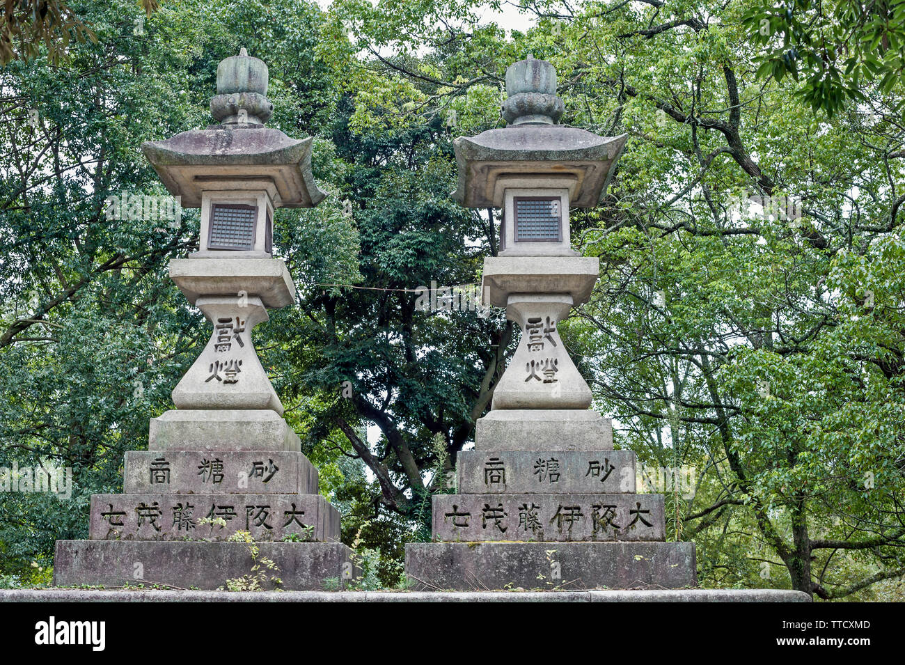 Two stone lanterns in the grounds of the Shinto Kasuga Taisha Shrine, Nara, Japan surrounded  by foliage from nearby trees Stock Photo