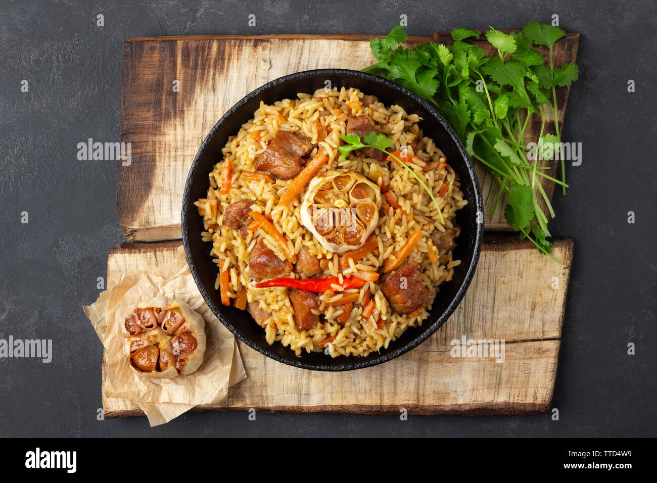 Oriental cuisine. Uzbek pilaf or plov from rice and meat in a cast iron pan on wooden rustic board. Top view. Stock Photo