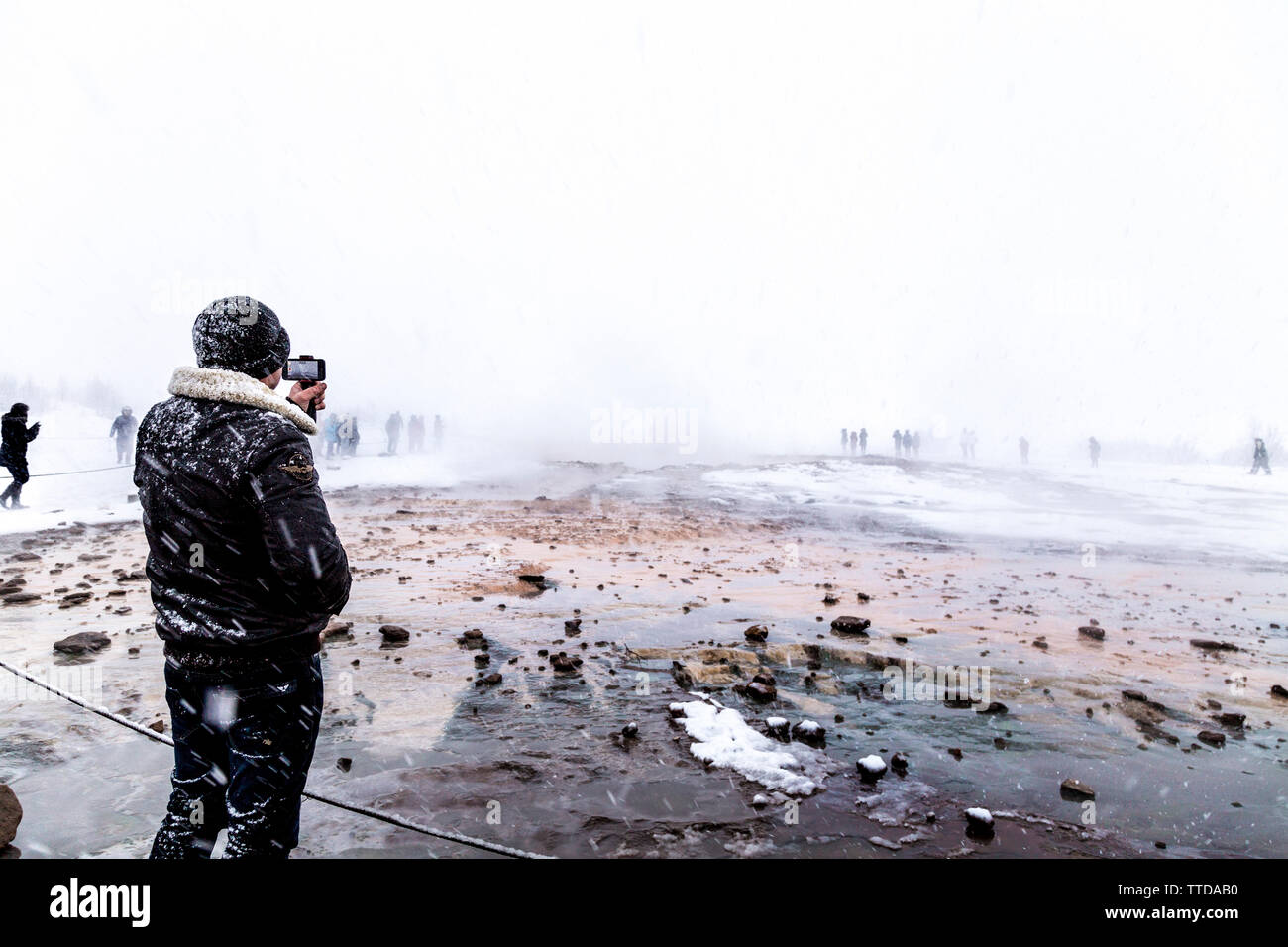 Man filming a geyser eruption in cold snowy weather, Geysir, Iceland Stock Photo