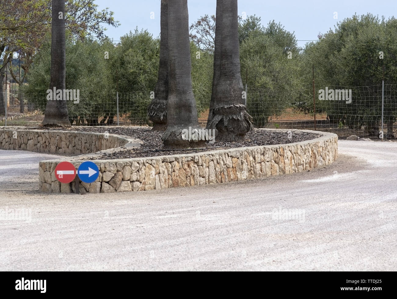 Circular road signs for direction and stone wall shape with trees in Mallorca, Spain. Stock Photo