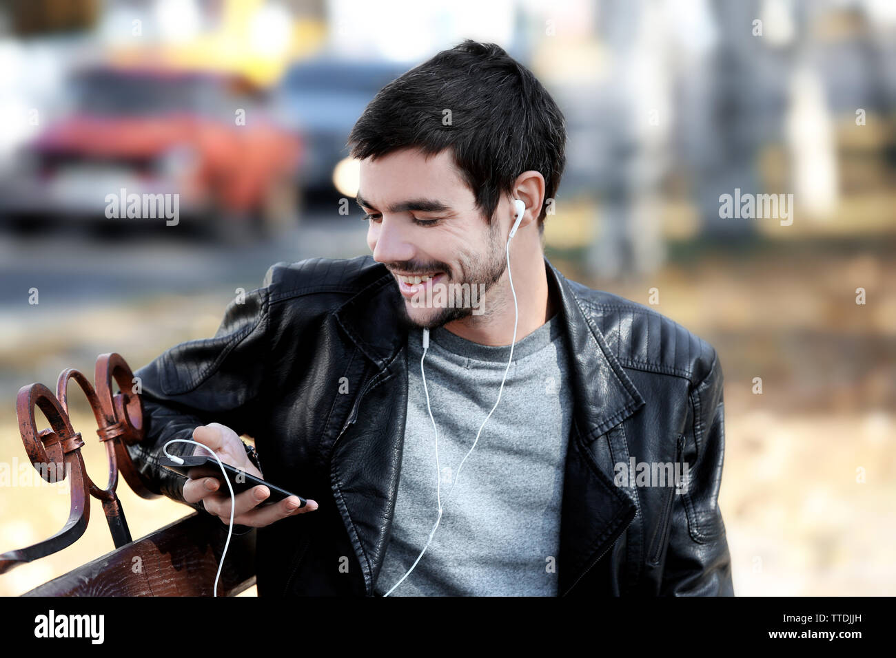 Young man sitting on a bench in park and listening to music Stock Photo ...