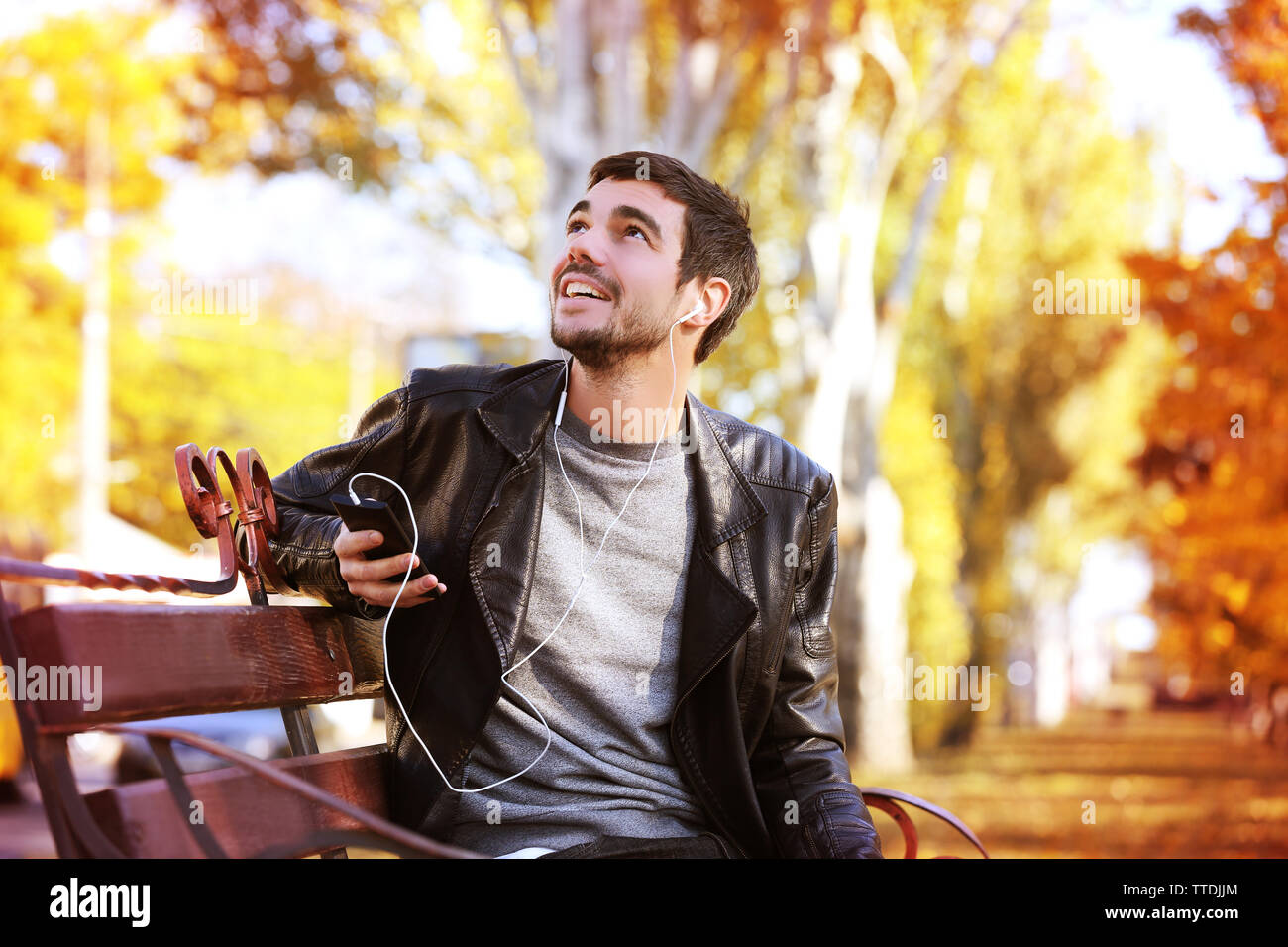 Young man sitting on a bench in park and listening to music Stock Photo ...