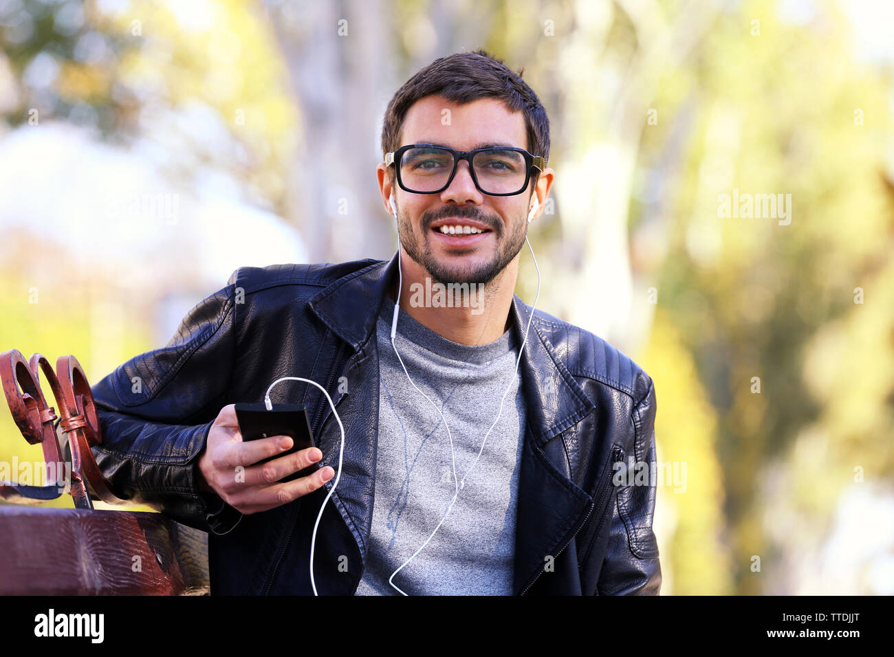 Young man sitting on a bench in park and listening to music Stock Photo ...