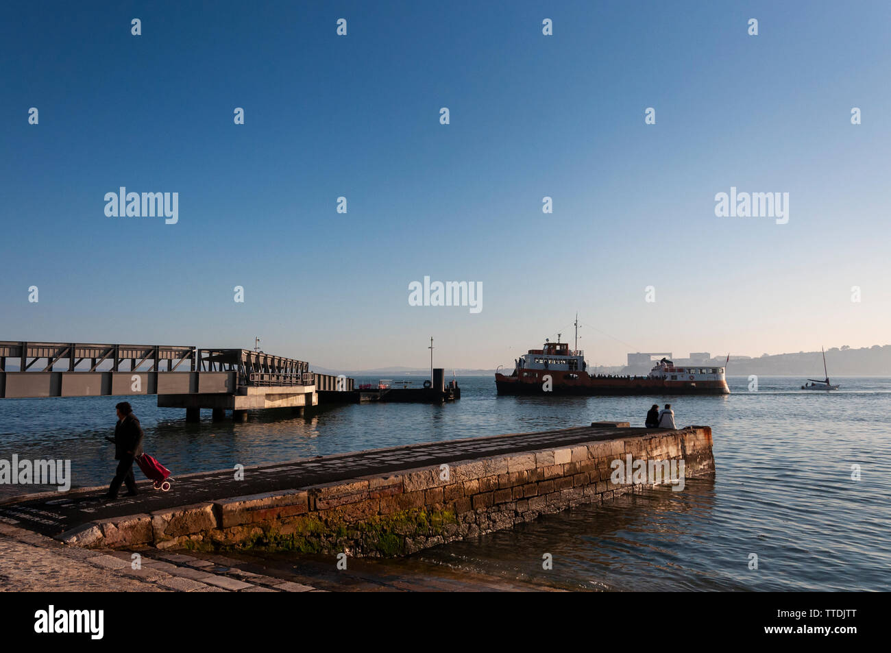 Lisbon, Portugal - January 22, 2012: View of the Cais do Sodre with a ferry boat (cacilheiro) arriving and people on a peer, in the city of Lisbon, Po Stock Photo