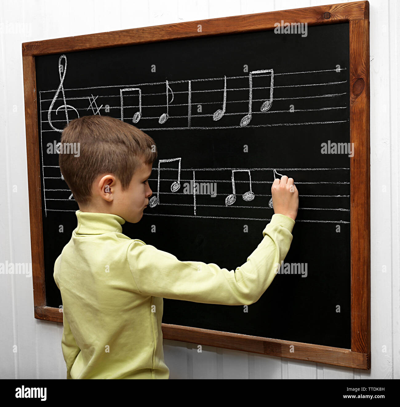 Boy Opening Note Cute boy writing at the blackboard with musical notes, in the classroom ...