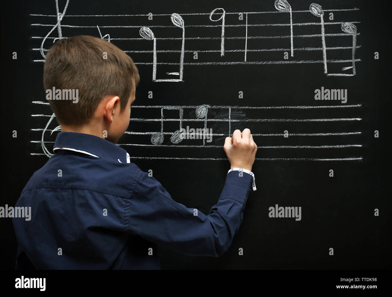 Boy Opening Note Cute boy writing at the blackboard with musical notes, in the classroom ...