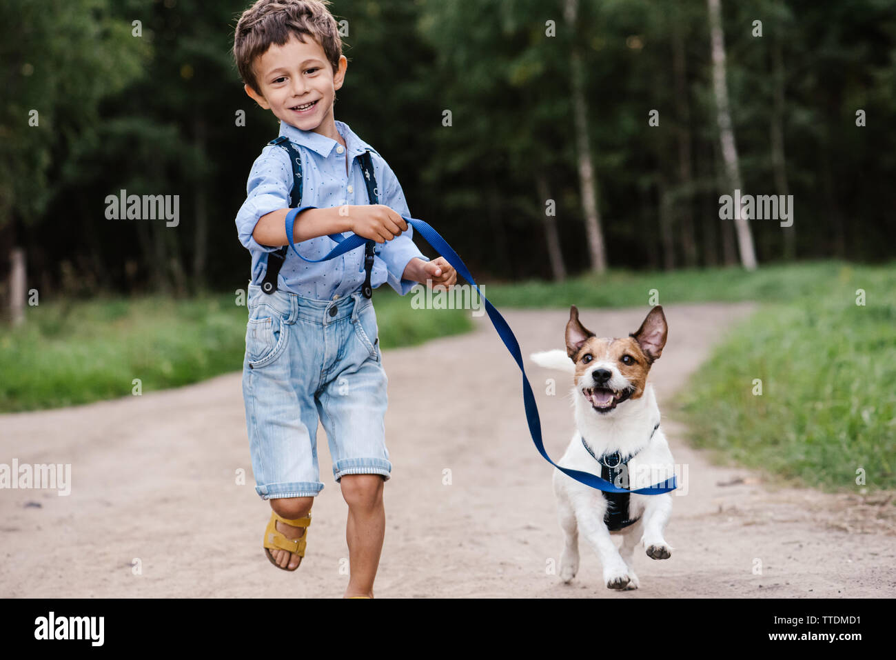 Happy boy with dog on leash running at country road Stock Photo