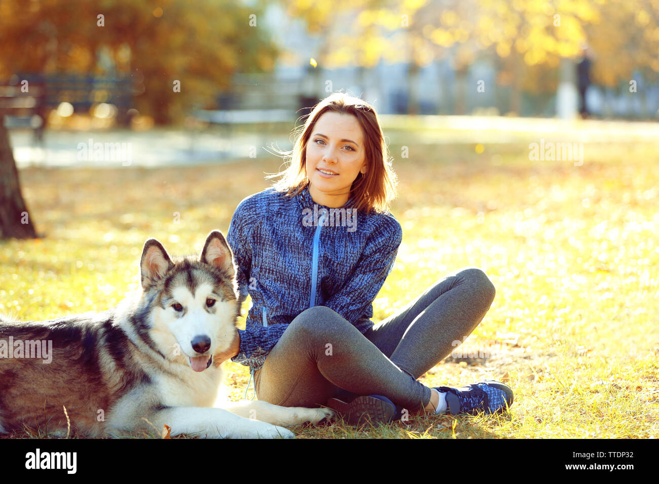 Happy young woman sitting with her dog on grass in park Stock Photo - Alamy