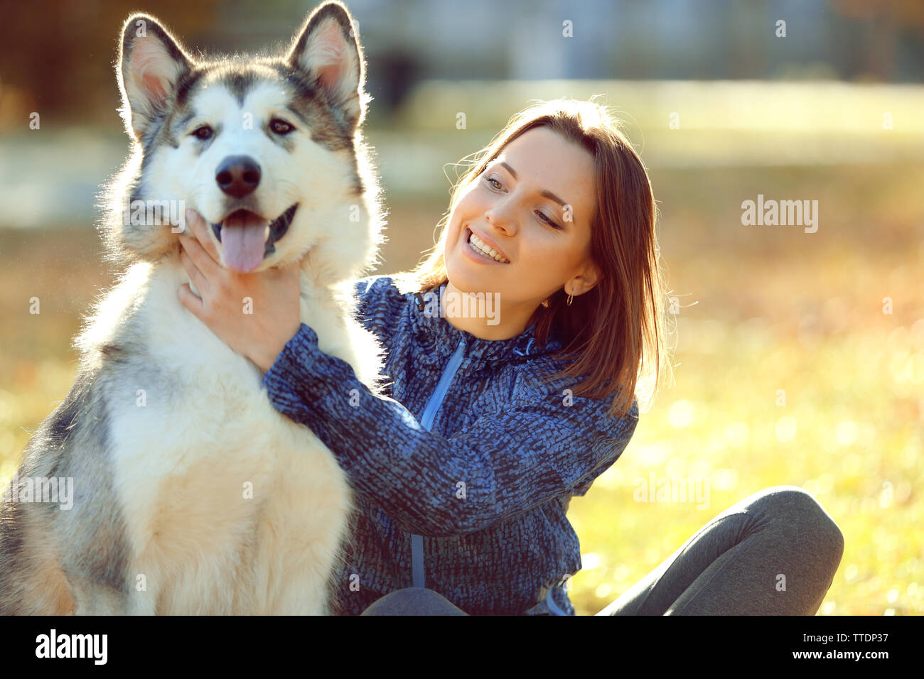 Happy young woman sitting with her dog on grass in park Stock Photo - Alamy