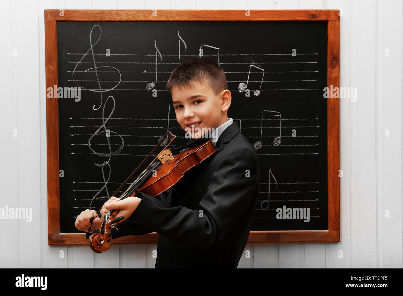 Young cute schoolboy playing the violin the blackboard with musical notes Stock Photo