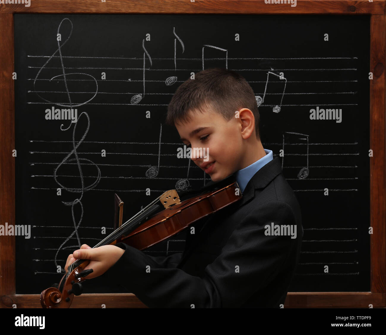 Young cute schoolboy playing the violin the blackboard with musical notes Stock Photo