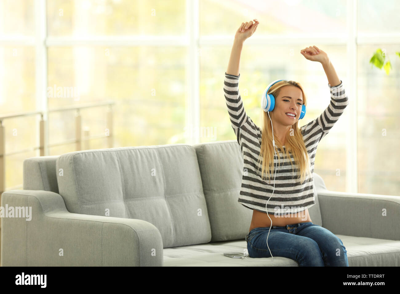 Young woman on a sofa listening to music Stock Photo - Alamy