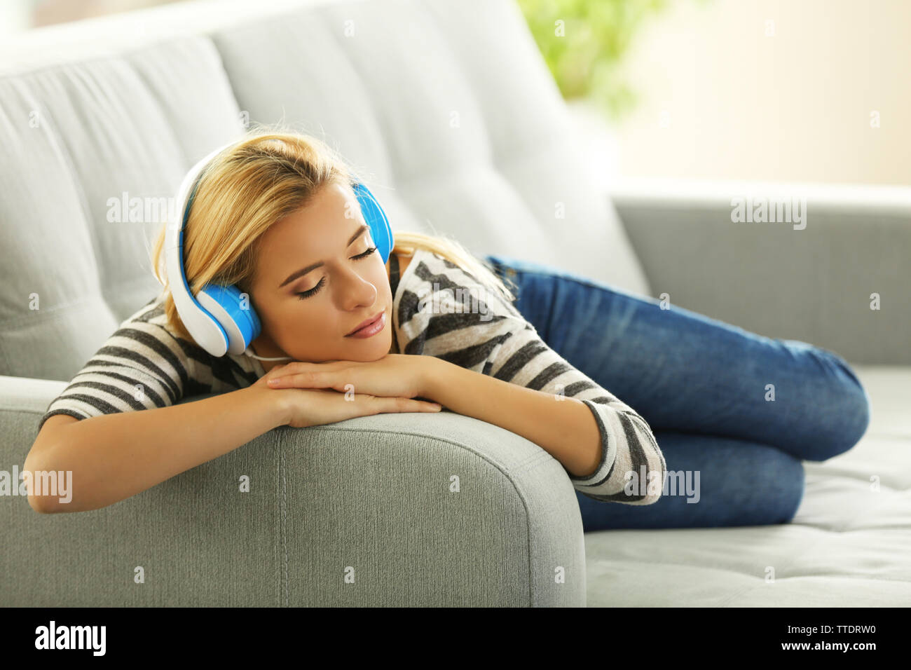 Young woman on a sofa listening to music Stock Photo - Alamy