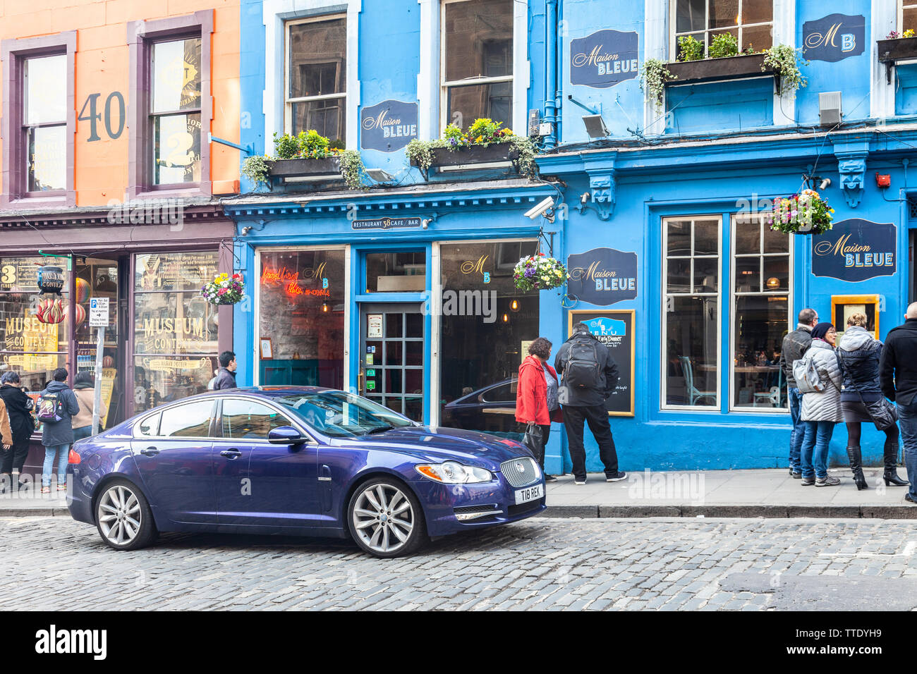 A dark blue Jaguar car parked outside Maison Bleue, a French restaurant in Victoria Street, Edinburgh, next to Museum Context, a Harry Potter shop. Stock Photo