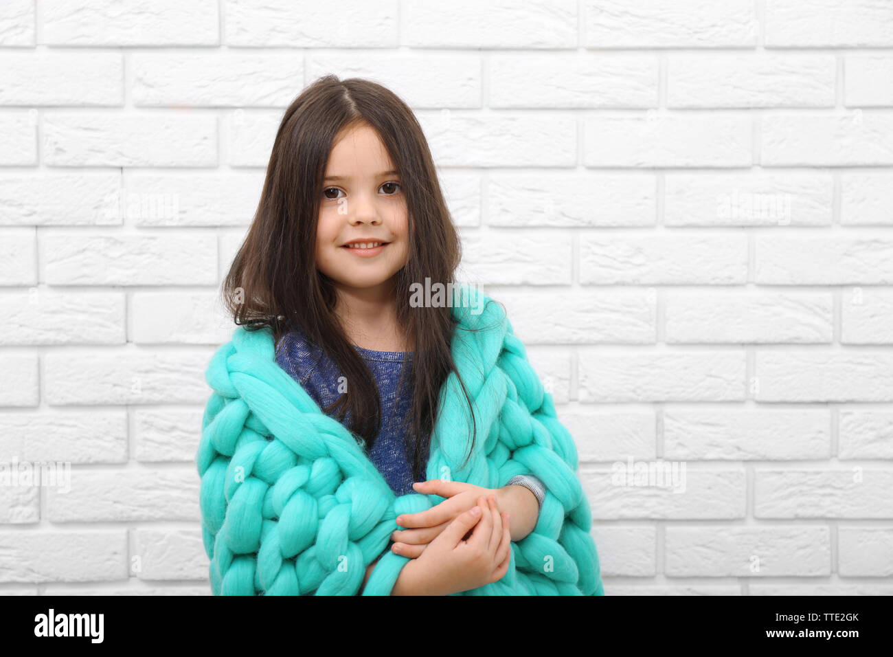 Little girl wrapped in blanket on a white brick wall background Stock