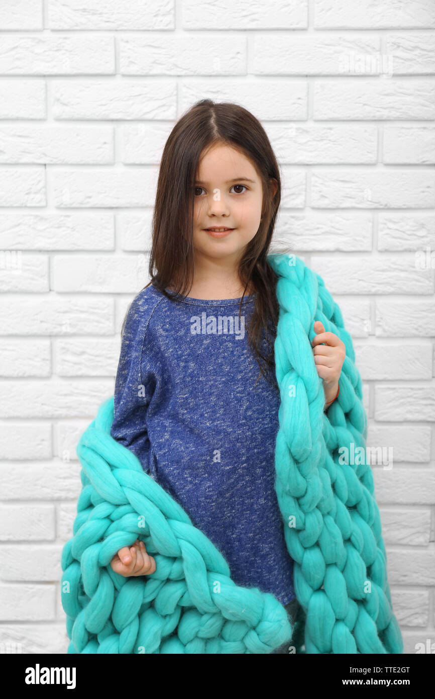 Little girl wrapped in blanket on a white brick wall background Stock