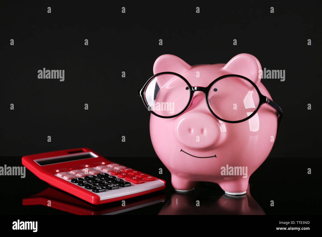 Piggy bank in glasses with calculator on dark background Stock Photo ...
