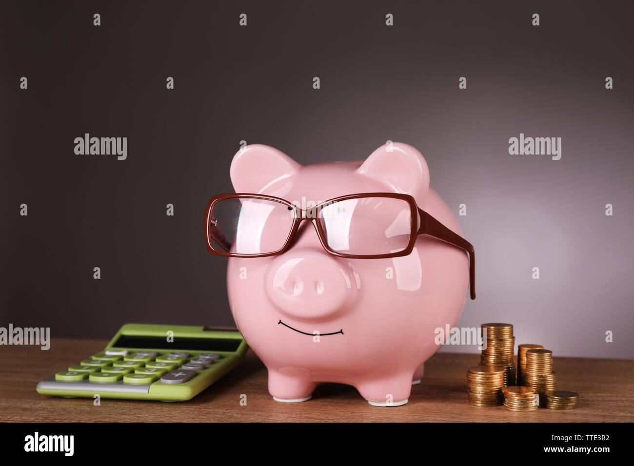 Piggy bank in glasses with calculator and coins on grey background ...