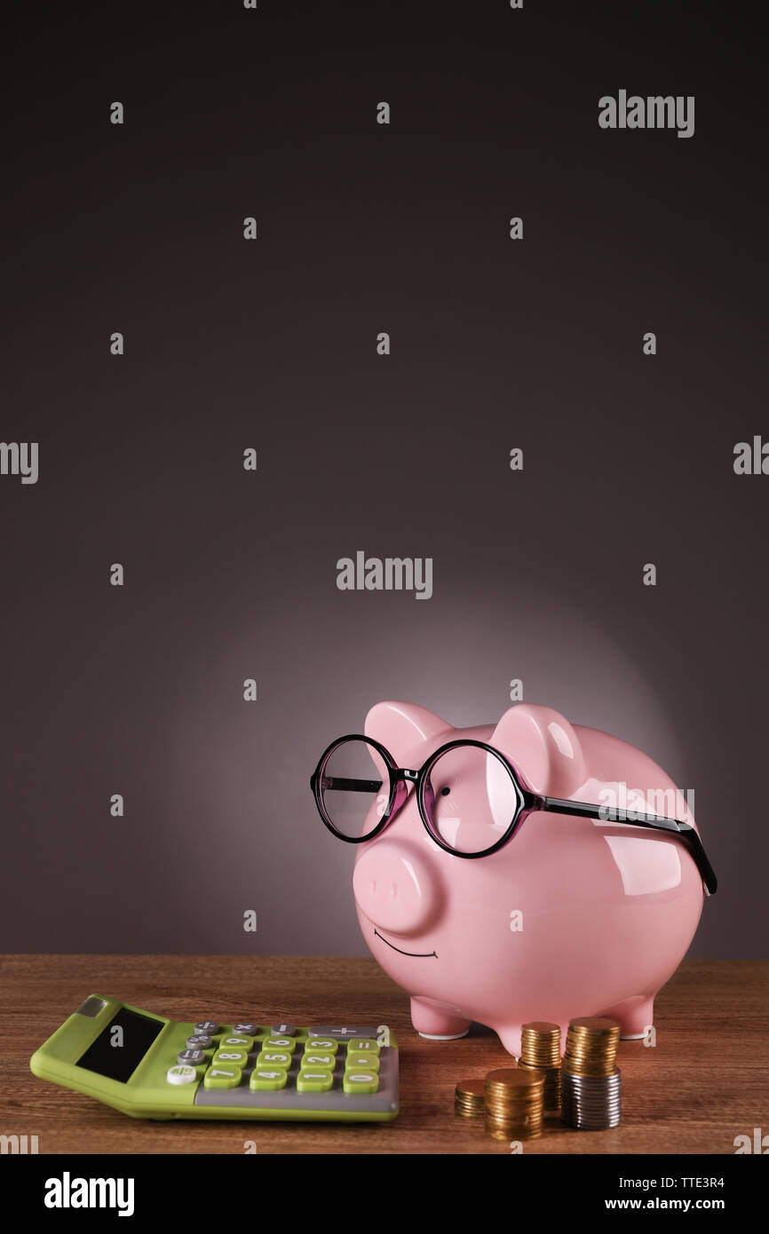 Piggy bank in glasses with calculator and coins on grey background ...