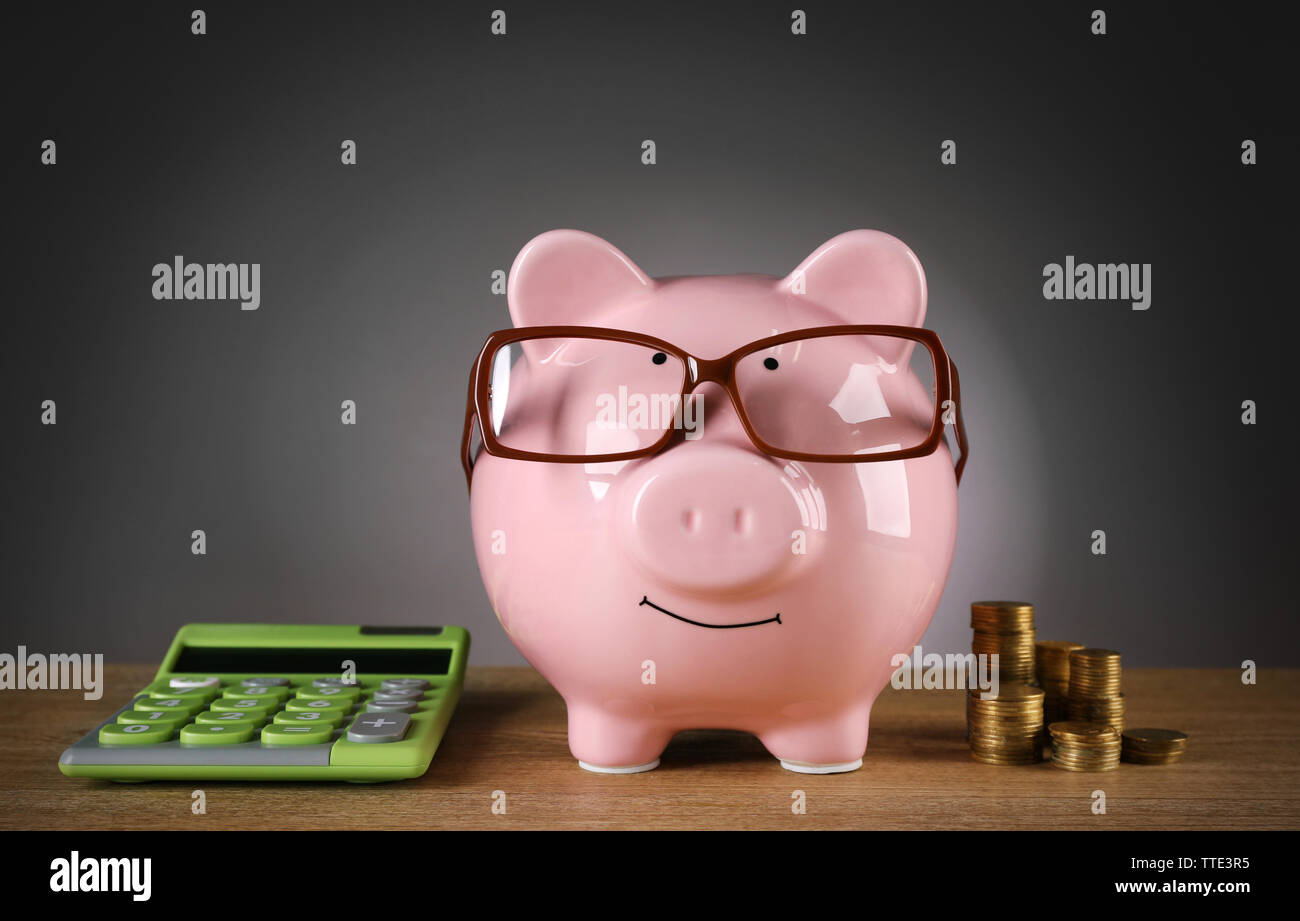 Piggy bank in glasses with calculator and coins on grey background ...