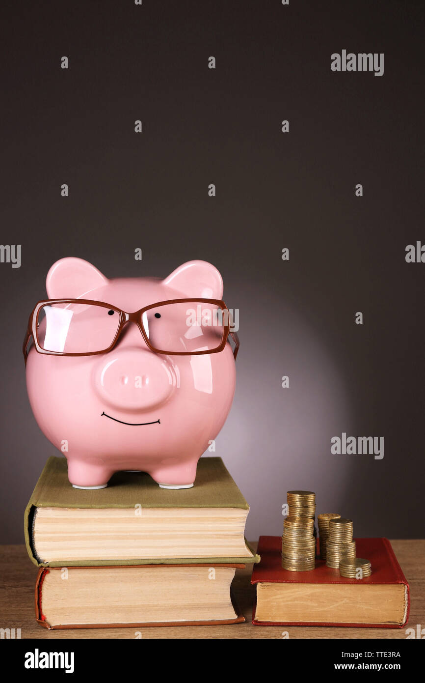 Piggy bank in glasses with books and coins on grey background Stock ...
