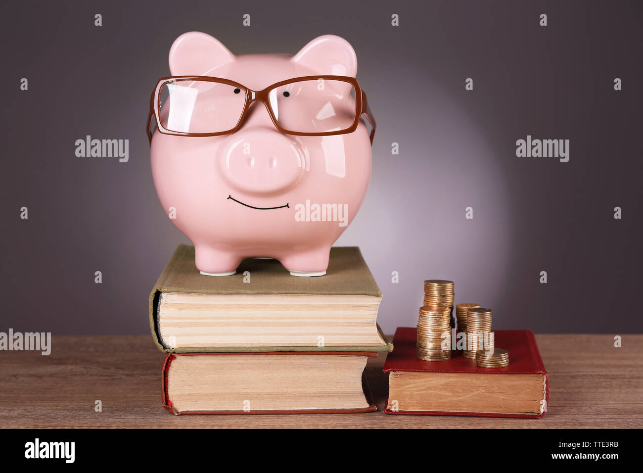 Piggy bank in glasses with books and coins on grey background Stock ...