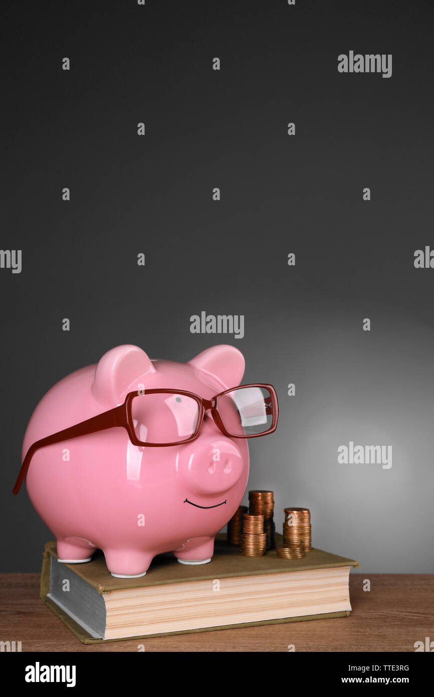 Piggy bank in glasses with book and coins on grey background Stock ...