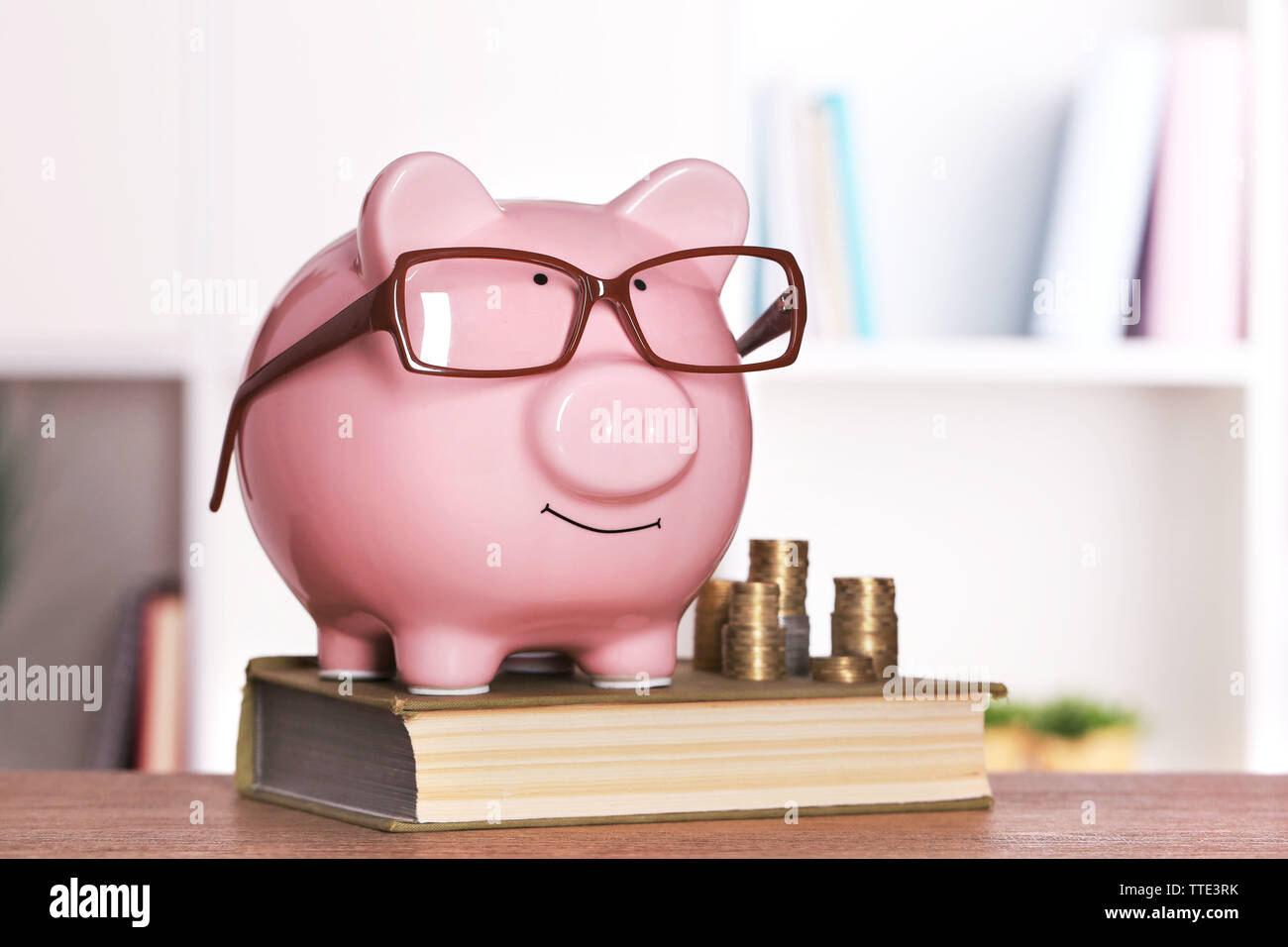 Piggy bank in glasses with book and coins on home or office background ...